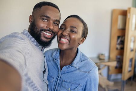 Smiling young African American couple taking a selfie at homeの写真素材