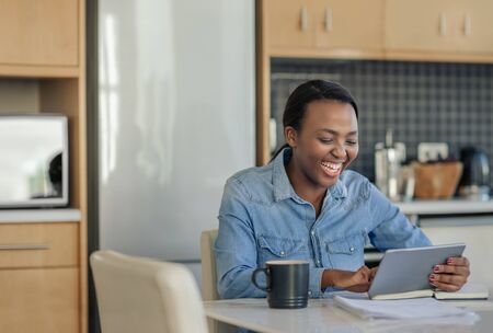 Laughing African American woman using a tablet in her kitchenの写真素材