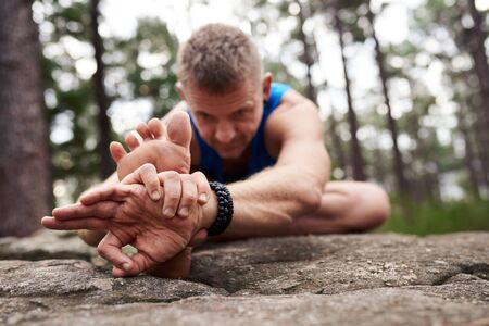 Man doing the head to knee yoga pose outdoorsの写真素材