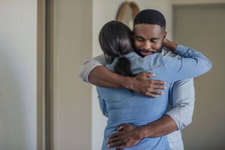 Affectionate young African American man hugging his wife at homeの写真素材