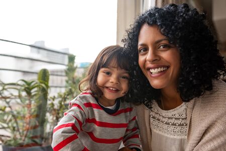 Smiling mother and her cute daughter sitting together at homeの写真素材