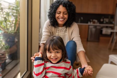 Smiling little girl and her mother sitting together at homeの写真素材