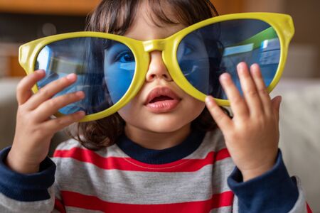 Adorable little girl playing with oversized novelty sunglasses at homeの写真素材