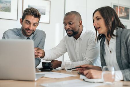 Smiling businesspeople working with a laptop during an office meetingの写真素材