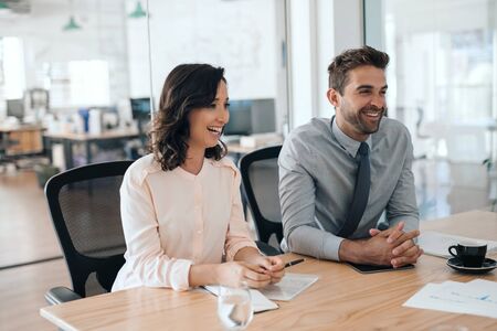 Two laughing businesspeople sitting together in an office boardroomの写真素材