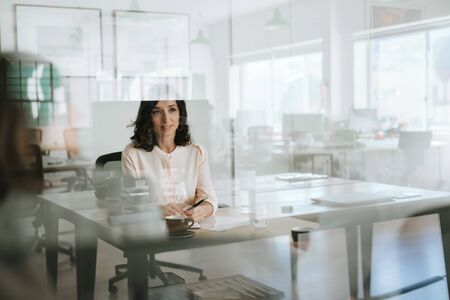 Smiling young businesswoman sitting inside of her officeの写真素材
