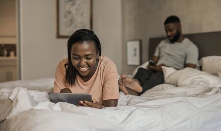 Smiling African American woman lying in bed using a tabletの写真素材