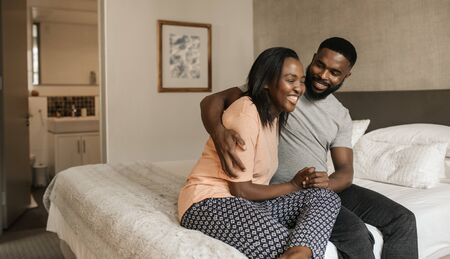 Young African American couple sitting on their bed and laughing togetherの写真素材