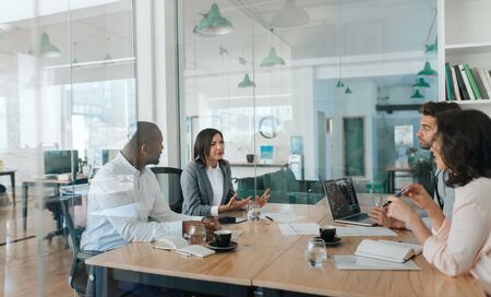 Diverse group of businesspeople talking together inside of an officeの写真素材