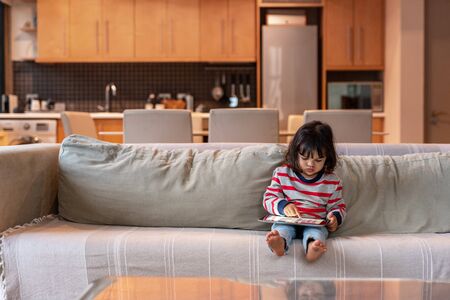 Cute little girl sitting on her sofa using a tabletの写真素材