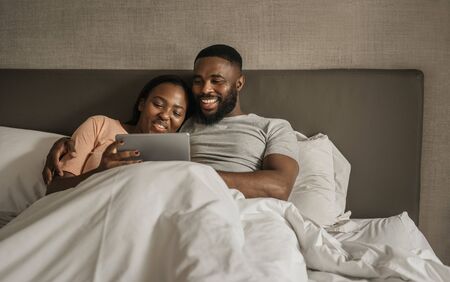 Smiling young African American couple using a tablet in bedの写真素材