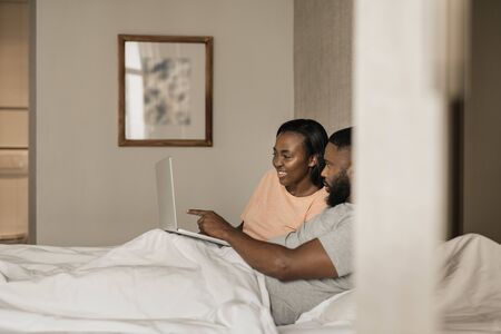Smiling young African American couple using a laptop in bedの写真素材