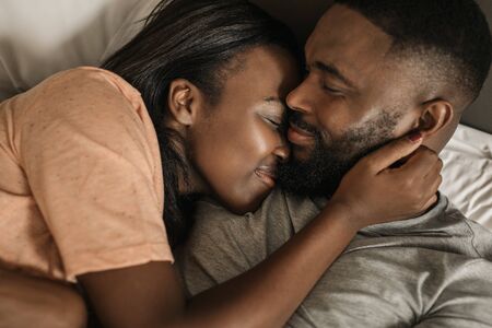 Smiling young African American couple hugging each other in bedの写真素材