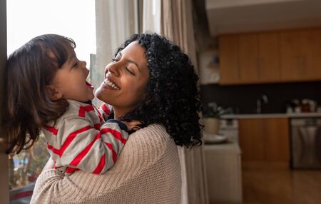 Loving mother hugging her laughing little daughter at homeの写真素材