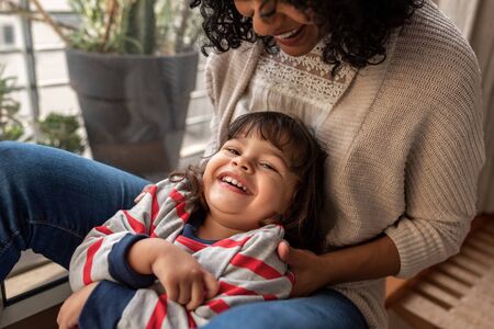 Smiling mother and adorable daughter playing together at homeの写真素材