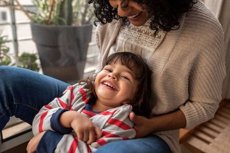 Smiling mother and adorable daughter playing together at home