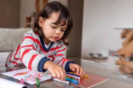 Adorable little girl coloring with crayons at homeの写真素材