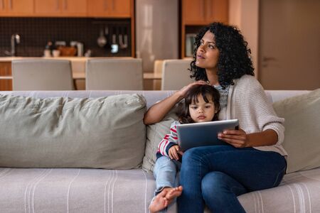 Mother using a tablet with her little daughter at homeの写真素材