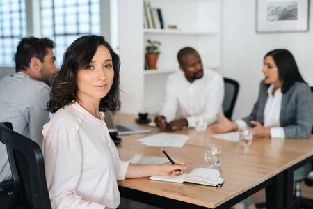 Smiling young businesswoman sitting with colleagues in a boardroomの写真素材