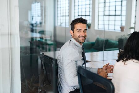 Smiling young businessman sitting with colleagues in a boardroomの写真素材