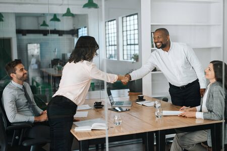 Smiling businessspeople standing in a boardroom shaking hands togetherの写真素材