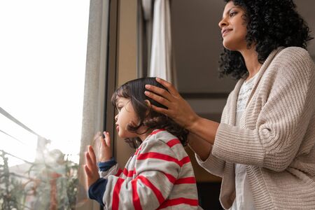 Little girl and her mother looking through a windowの写真素材