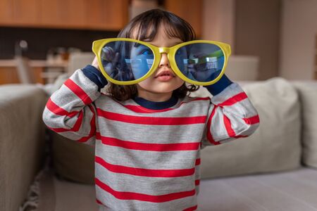 Cute little girl playing with oversized novelty sunglasses at homeの写真素材