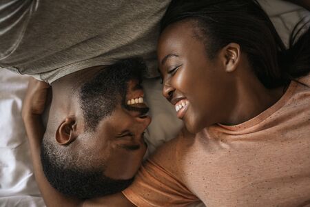 Affectionate young African American couple laughing together in bedの写真素材