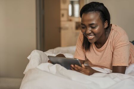 Smiling African American woman lying in bed using a tabletの写真素材