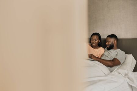 Smiling African American couple lying in bed using a laptopの写真素材
