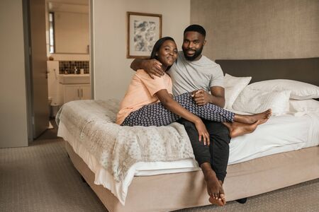 Smiling young African American couple sitting together on their bed