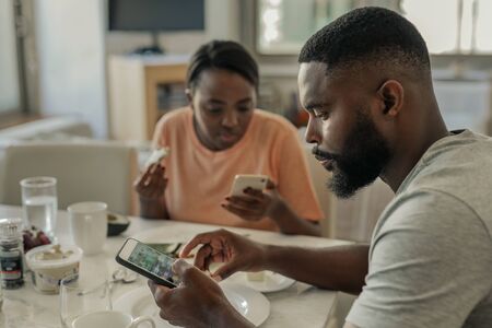 Young African American couple distracted from breakfast by their cellphonesの写真素材