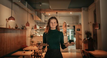 Smiling waitress carrying food orders in a bistro at nightの写真素材