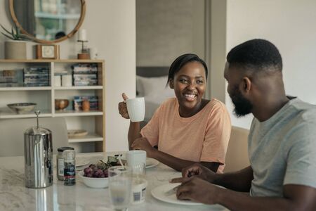 Laughing young African American couple enjoying breakfast together at homeの写真素材