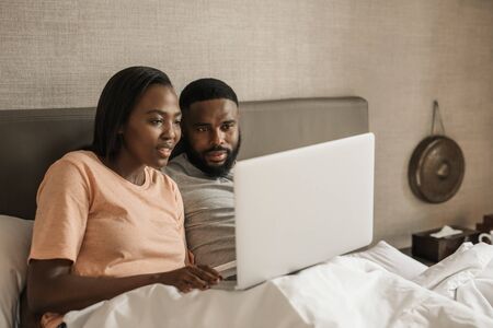 Young African American couple using a laptop together in bedの写真素材