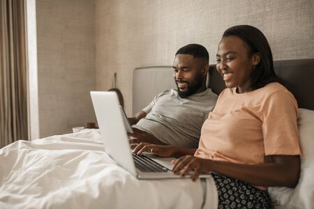 African American couple using a tablet and laptop in bedの写真素材