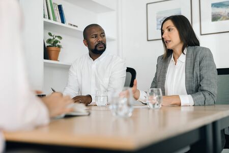 Two businesspeople talking with a colleague at an office tableの写真素材