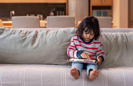 Little girl sitting on her sofa using a digital tabletの写真素材