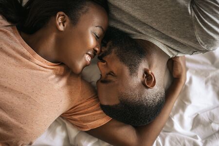 Loving young African American couple lying in bed togetherの写真素材