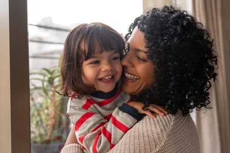 Loving mother hugging her cute little daughter at homeの写真素材