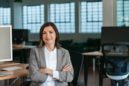 Smiling businesswoman sitting at her office desk in the afternoonの写真素材