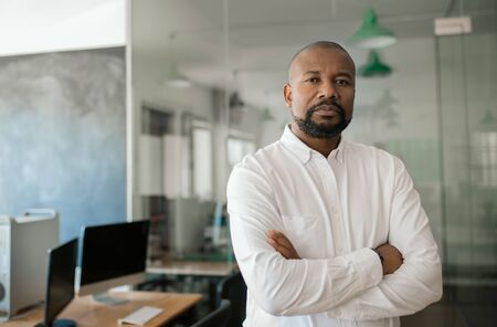 Mature African American businessman standing alone in a large officeの写真素材