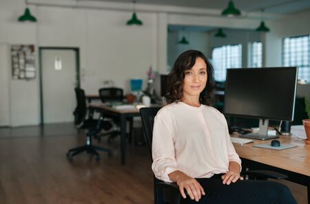 Smiling businesswoman sitting at her office desk in the afternoonの写真素材