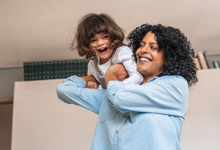 Laughing mom and cute little daughter playing at homeの写真素材