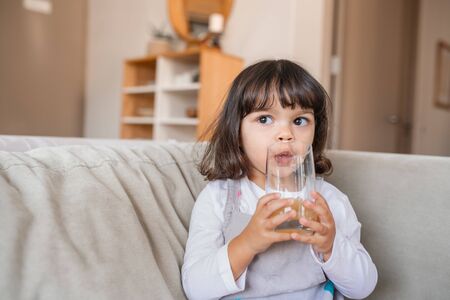 Addorable little girl drinking juice at homeの写真素材