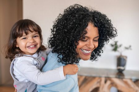 Laughing mother piggybacking her cute daughter around the houseの写真素材