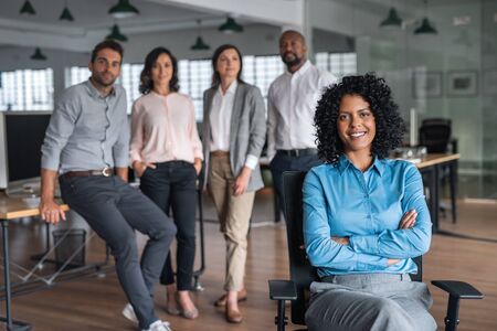 Smiling businesswoman sitting in an office with colleagues behind herの写真素材
