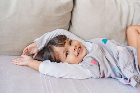 Portrait of a cute little girl smiling while playing on a sofa in her living room at home