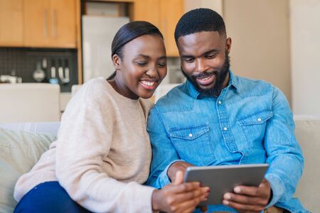 Smiling African American couple using a tablet on their sofaの写真素材