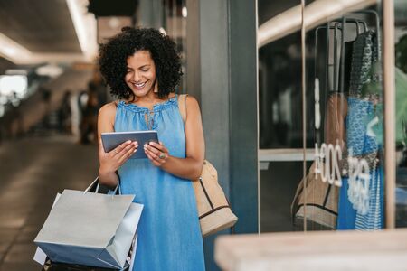 Young woman smiling and using a tablet while out shoppingの写真素材